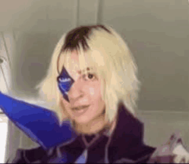 a woman with blonde hair and a blue eye is wearing a wig and a costume .