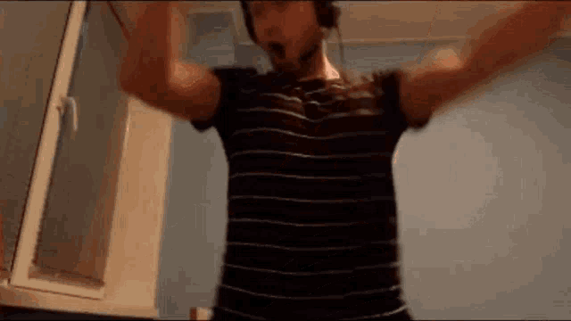 a man wearing headphones and a striped shirt is dancing in a room with his arms outstretched .