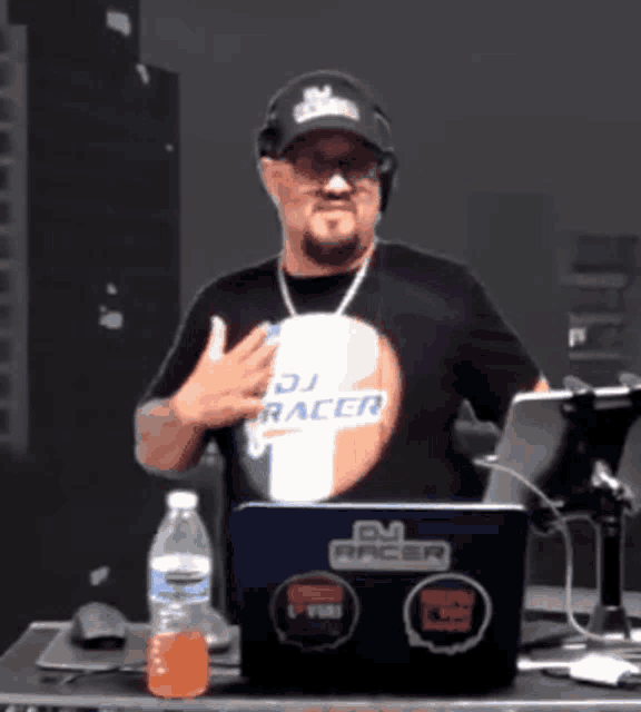 a man wearing a dj racer shirt stands in front of his laptop
