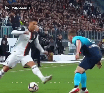 a soccer player is kicking a soccer ball while another player tries to block him .