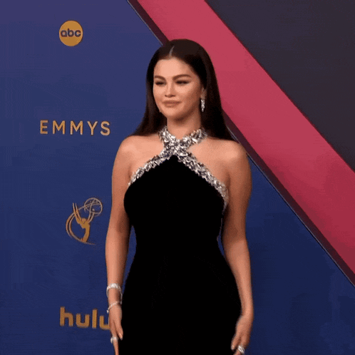 a woman in a black dress is standing in front of a emmys logo