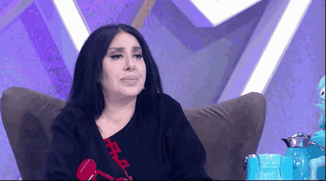 a woman in a black shirt with a red chain around her neck is sitting on a couch