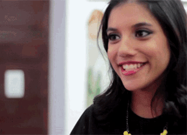 a woman in a black shirt and yellow necklace smiles