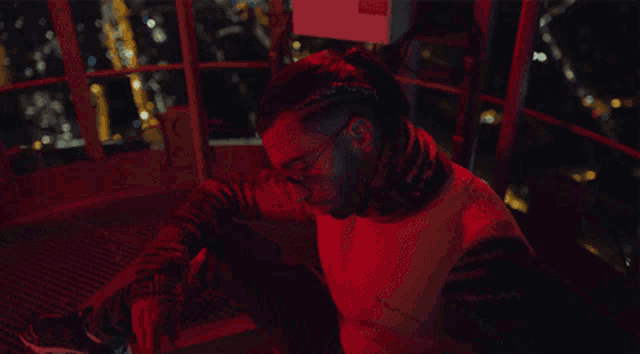 a man sitting on a balcony with a red light behind him that says ' emergency ' on it