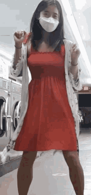 a woman in a red dress is wearing a mask and dancing in a laundromat .