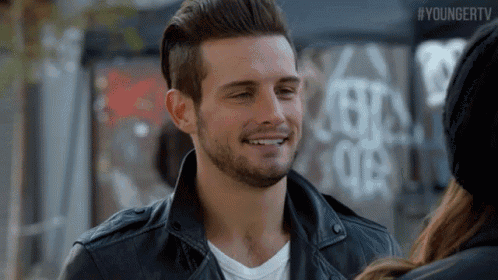 a man with a beard wearing a leather jacket is smiling at a woman .