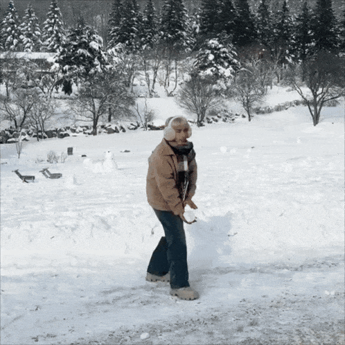 a man wearing ear muffs is shoveling snow in a snowy field