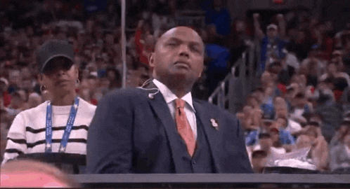 a man in a suit and tie is sitting in the stands watching a game .