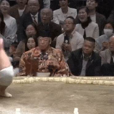 a man in a kimono is sitting in front of a crowd of people .