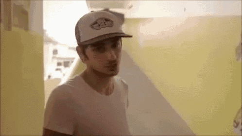 a man wearing a white hat and a white t-shirt is standing in a room .