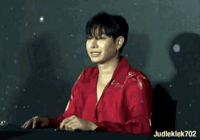 a man in a red shirt is sitting at a table with his hands folded