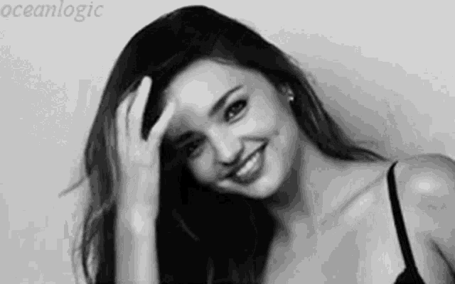 a black and white photo of a woman in a bra smiling and touching her face .