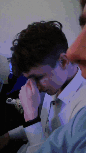 a man covering his face with his hand while another man watches