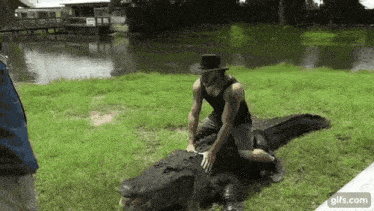 a man in a hat is kneeling on top of an alligator .
