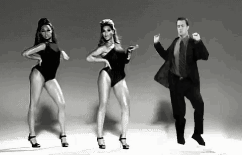 a man in a suit and tie is dancing with two women in swimsuits .