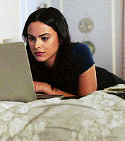 a woman is laying on a bed looking at a laptop