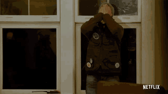a man covering his face in front of a window with netflix written on the bottom right