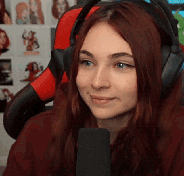 a woman wearing headphones and a red and black chair smiles in front of a microphone