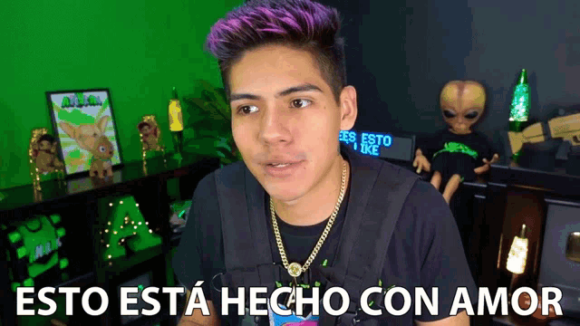 a man with purple hair is standing in front of a green screen that says " esto esta hecho con amor "