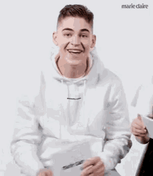 a man in a white hoodie is smiling and holding a piece of paper .