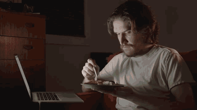 a man is eating a plate of food in front of a laptop computer