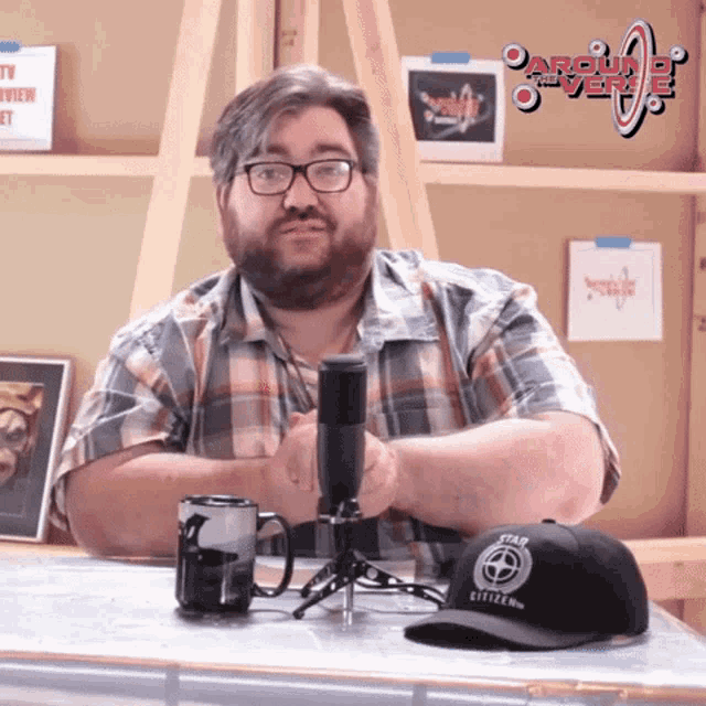 a man wearing glasses and a plaid shirt is sitting in front of a microphone with a hat that says star citizen