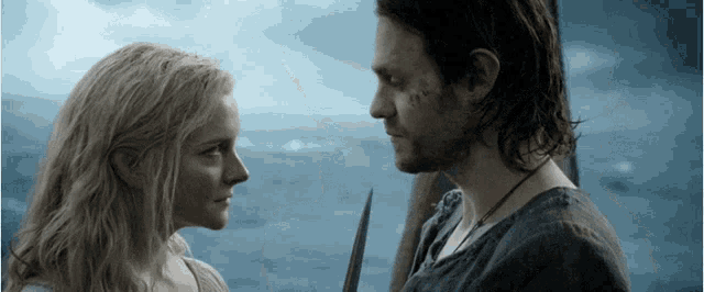 a man and a woman are looking at each other in front of a body of water