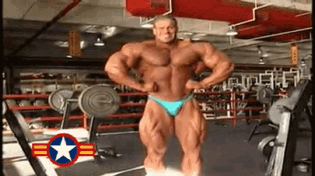 a man in a blue bikini is standing in a gym with a star in the corner