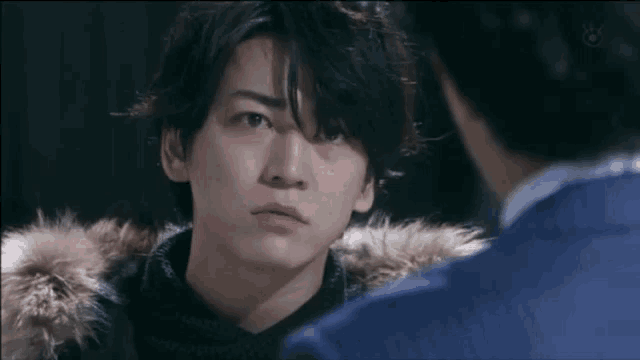 a man in a fur coat is looking at another man in a blue jacket .