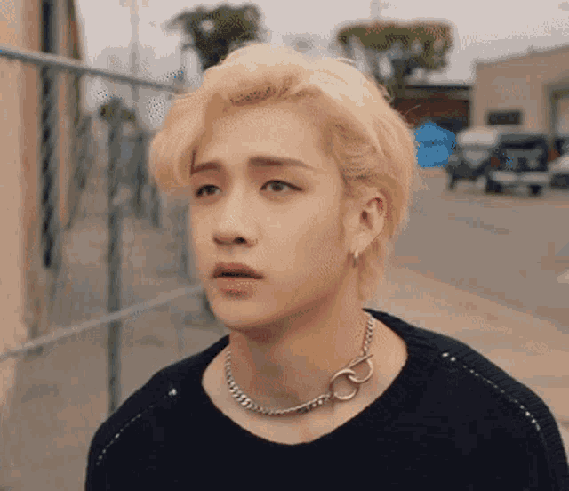 a young man with blonde hair wearing a black sweater and a necklace
