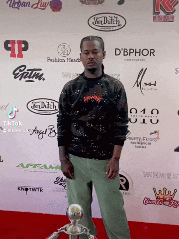 a man stands in front of a wall of logos including d' bphor and von dutch