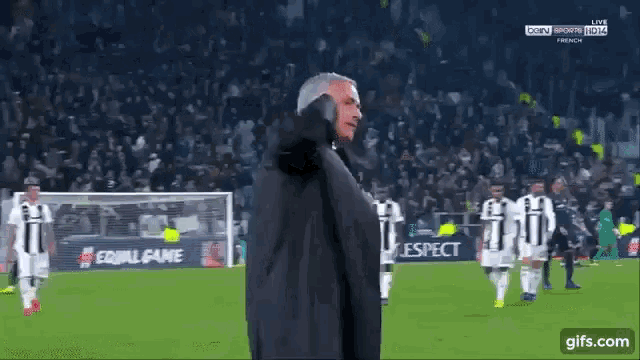 a man in a black jacket stands on a soccer field
