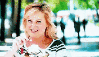 a woman is eating ice cream and smiling while sitting on a sidewalk .