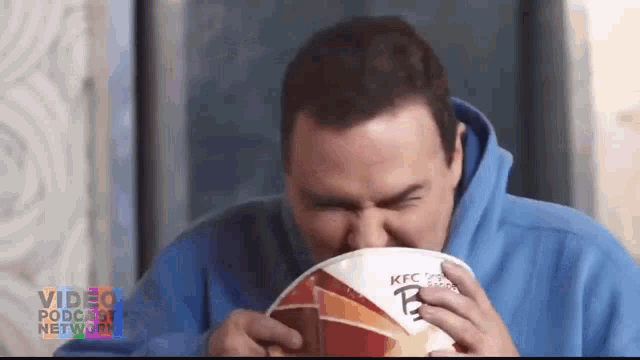 a man in a blue hoodie is eating a bag of kfc nuggets