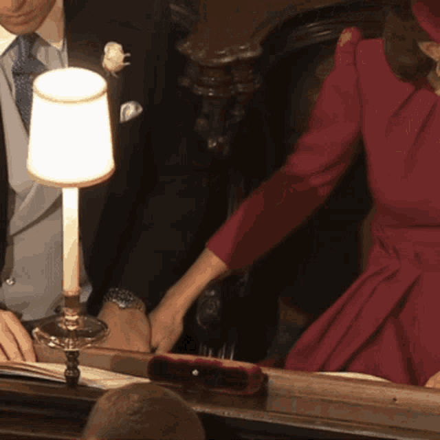 a woman in a red dress is holding a man 's hand in front of a lamp