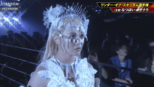 a woman in a white dress with a crown on her head is standing in front of a sign that says stardom