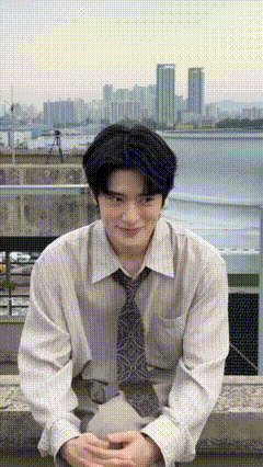 a man wearing a white shirt and tie is sitting on a ledge with a city in the background