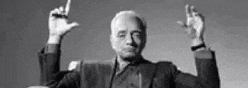 a black and white photo of a man in a suit holding his hands up in the air .