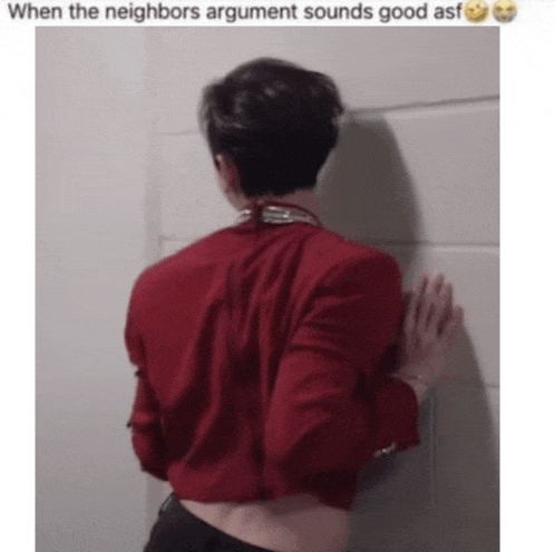 a man in a red shirt is leaning against a wall with his back to the camera .