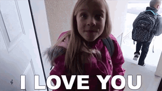 a little girl in a pink jacket is standing in front of a door and says i love you