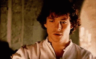 a man with curly hair and a white shirt is looking at the camera .