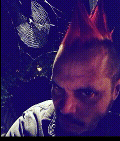 a man with a mohawk looks at the camera with a rocket in the background