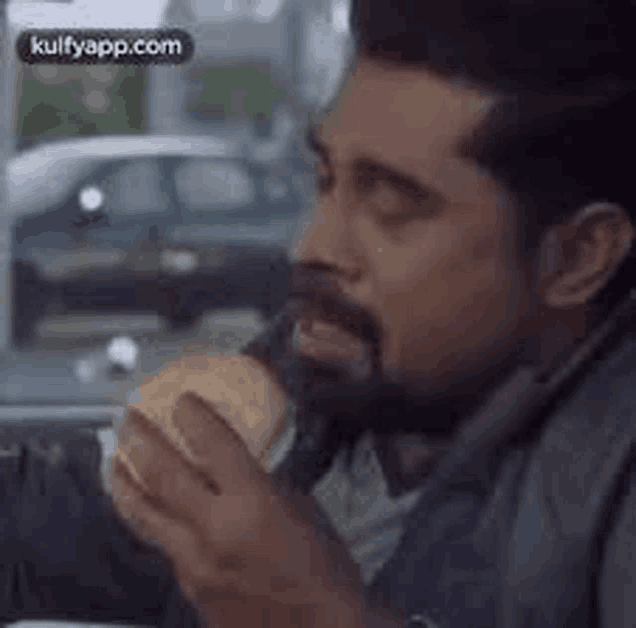 a man with a beard is eating a hamburger in the back seat of a car .