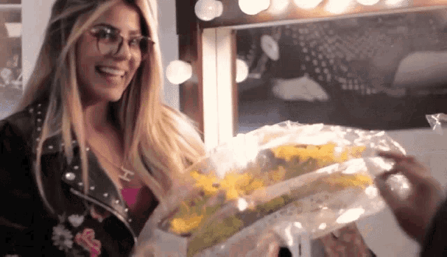 a woman wearing glasses is smiling while holding a bouquet of yellow flowers
