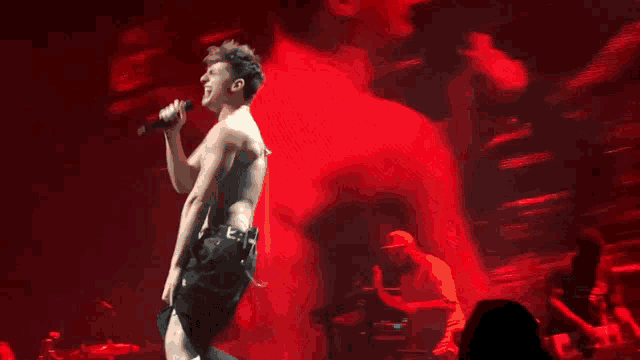 a shirtless man is singing into a microphone on stage