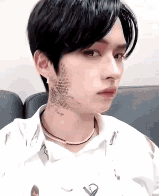a young man with a tattoo on his face is sitting in a chair .