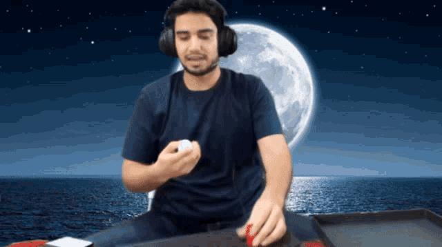 a man wearing headphones sits in front of a full moon over the ocean