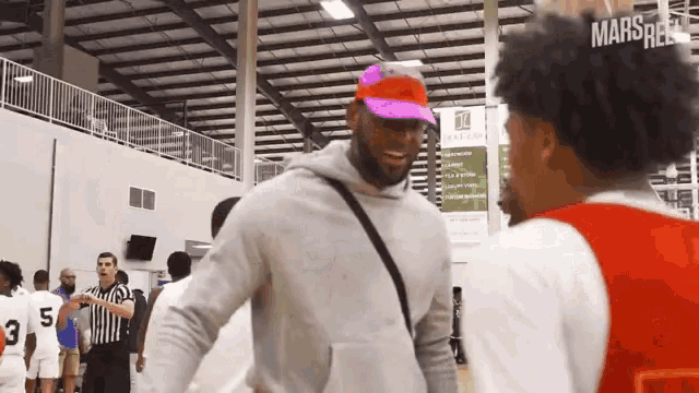 a man wearing a pink hat talks to another man