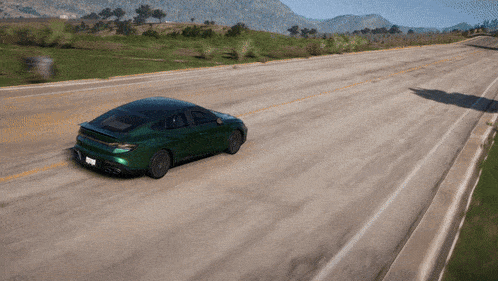 a green car is driving down a road with mountains in the distance