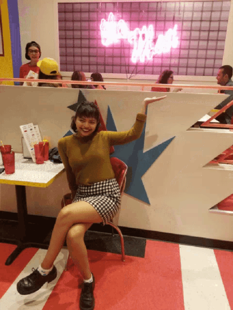 a woman sits in a chair in front of a sign that says shake n ' shake